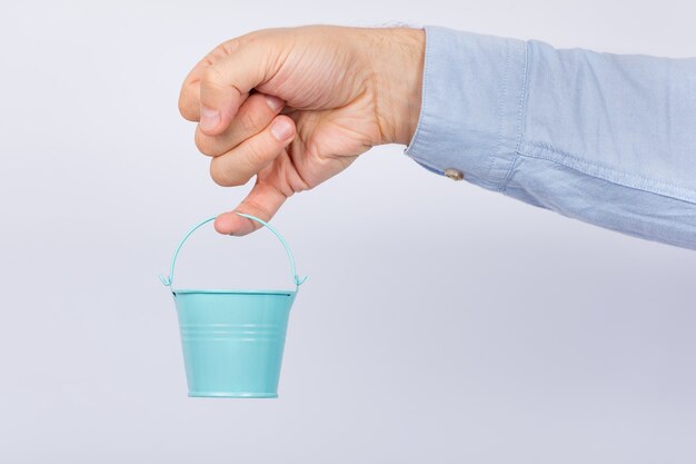 Man with little finger holding small toy bucket on white background.