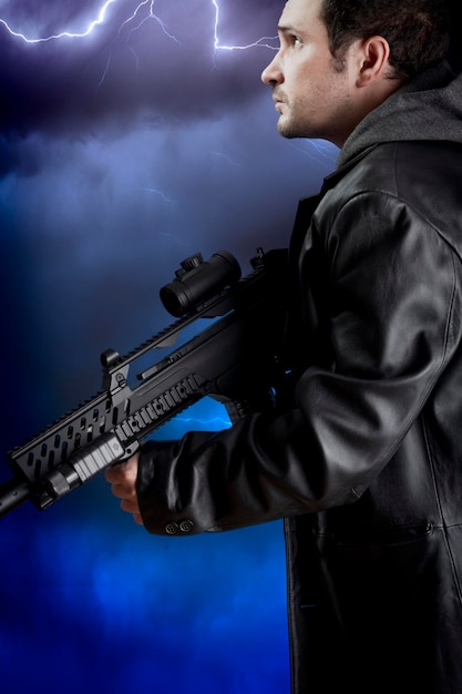 Man with long leather jacket and assault rifle over storm background