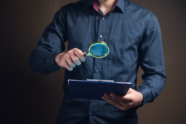 A man with a magnifying glass looks at papers on a brown surface