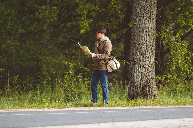 Man with map and bag in hand walking on a roadside