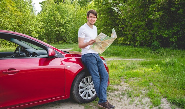 The man with the map in hand standing next to a car in the forest.