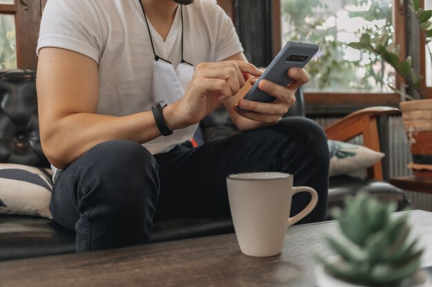 マスクをした男がスマホを使ってカフェでコーヒーを飲む