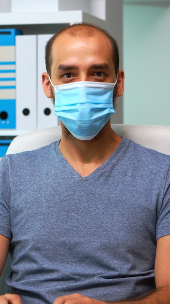 Man with mask working at computer and looking at camera sitting in office during pandemic. Entrepreneur in new normal personal workplace corporate writing on computer keyboard looking at desktop