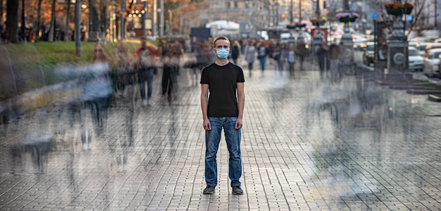 The man with medical face mask stands on the crowded urban street