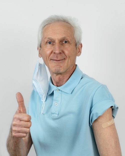 Photo man with medical mask showing thumbs up with bandage on arm after vaccine shot