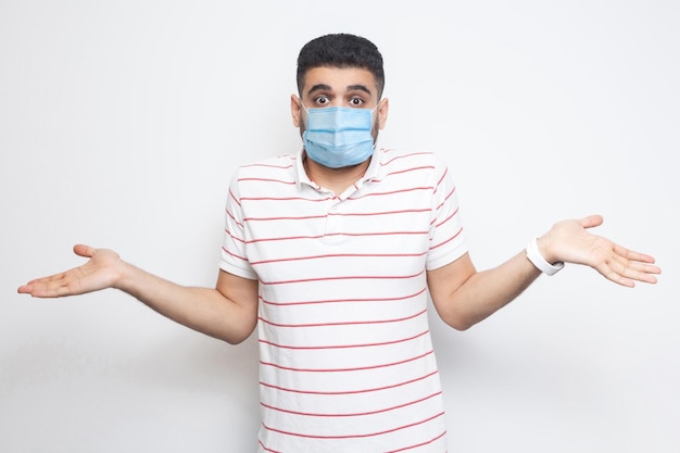 Man with medical mask in striped tshirt standing with raised arms and dont know what to do