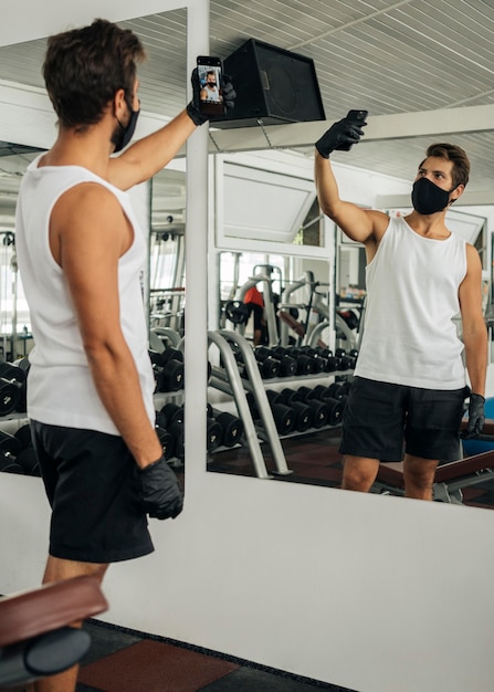 Uomo con mascherina medica prendendo un selfie in palestra