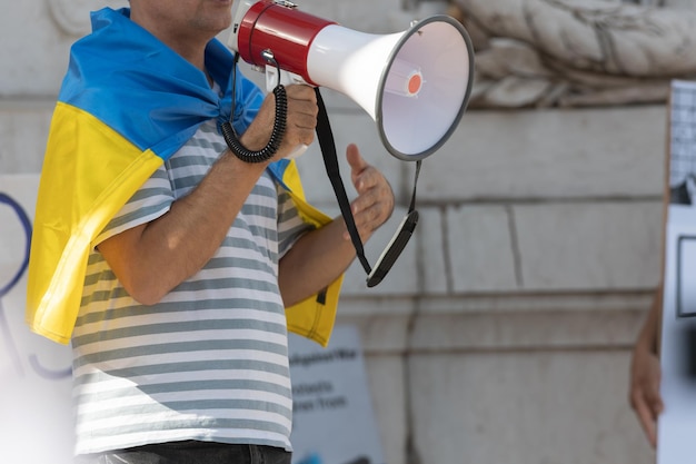 Photo a man with a megafon carries a ukrainian flag on his shoulders at the rally