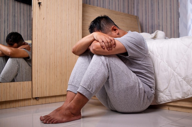 мужчина с проблемами психического здоровья сидит на полу с рукой на лице и чувствует стресс
