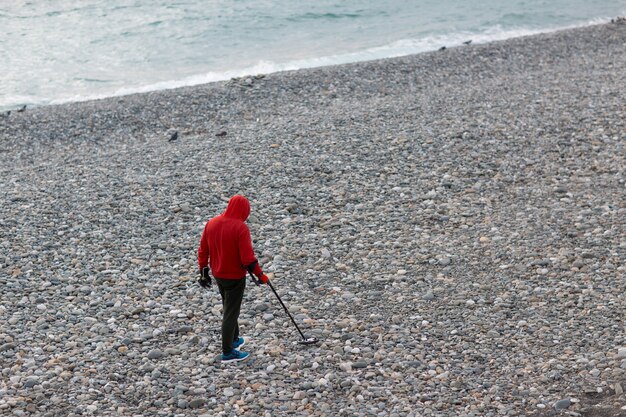 L'uomo con un metal detector sta cercando monete e gioielli sulla spiaggia