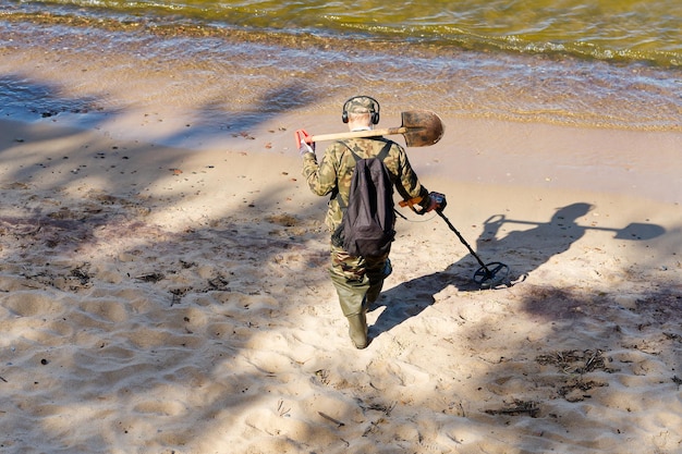 Мужчина с металлоискателем идет у кромки воды песчаного пляжа.