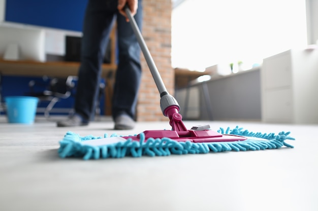 Man with mop washes floor in office. Cleaning company services concept