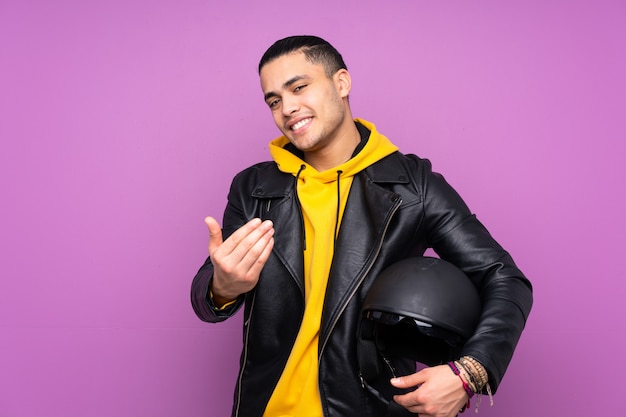 Man with a motorcycle helmet isolated on purple wall inviting to come