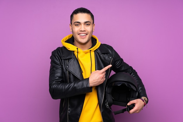 Man with a motorcycle helmet isolated on purple wall pointing finger to the side