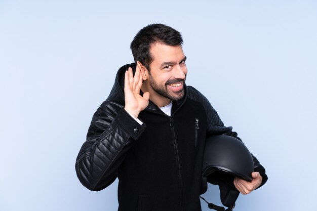 Uomo con un casco del motociclo sopra la parete isolata che ascolta qualcosa mettendo la mano sull'orecchio