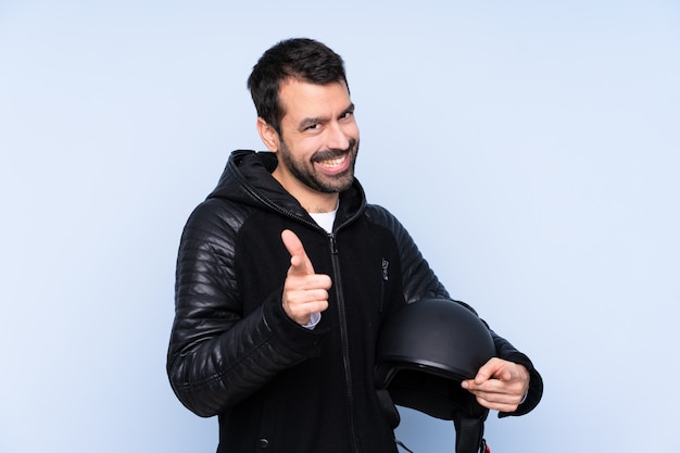 Man with a motorcycle helmet over isolated wall pointing to the front and smiling