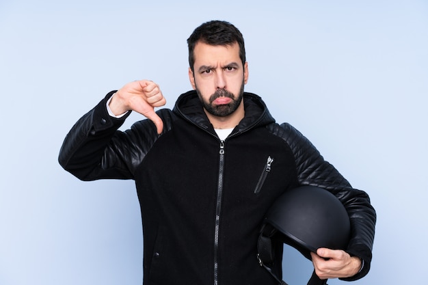 Man with a motorcycle helmet over isolated wall showing thumb down