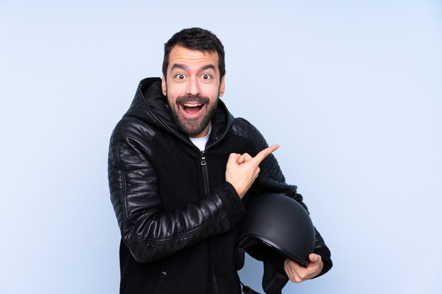 Man with a motorcycle helmet over isolated wall surprised and pointing side