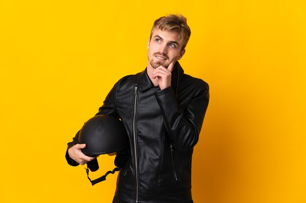 Man with a motorcycle helmet isolated on yellow thinking an idea while looking up