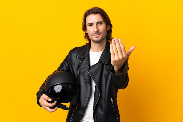 손으로와 서 초대 노란색 벽에 고립 된 오토바이 헬멧을 가진 남자. 당신이 와서 행복