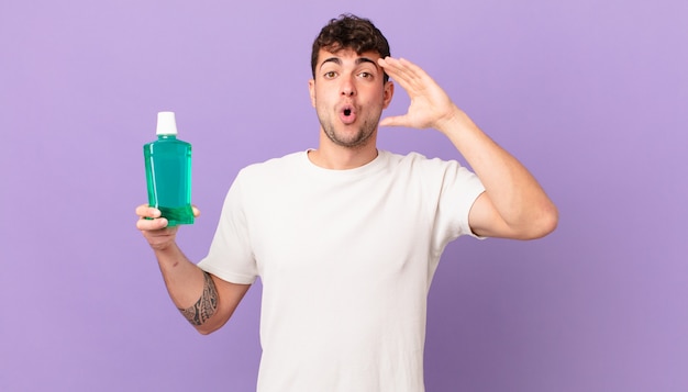 Man with mouthwash looking happy, astonished and surprised, smiling and realizing amazing and incredible good news