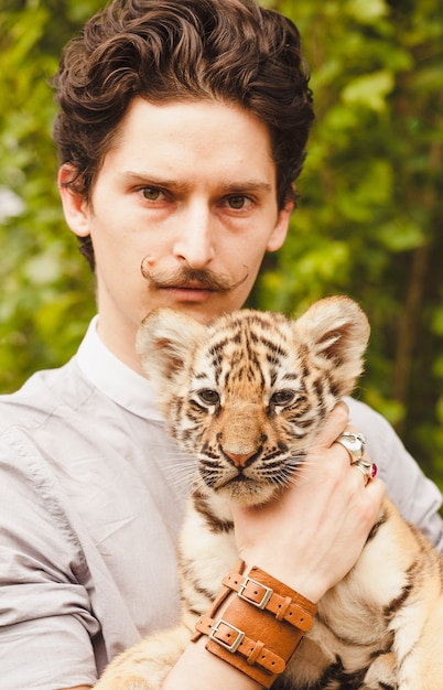 A man with a mustache looks into the face of a tiger cub otdoors