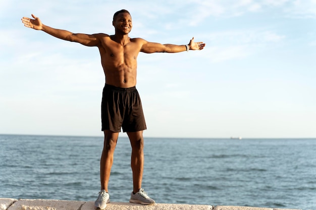 Man with naked torso celebrating victory or good results while standing near the sea