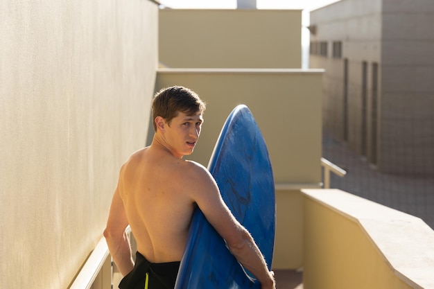 A man with naked torso holding a surfboard looking over his shoulder