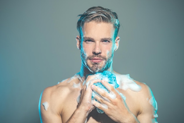 Man with naked torso is washed in shower muscular guy covered with foam handsome bearded macho