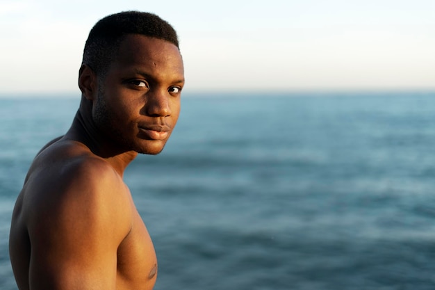 Man with naked torso standing on the beach and looking at the camera while warming at the sun