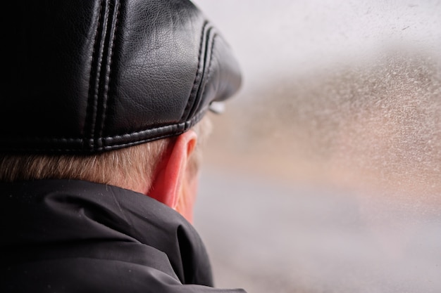 A man with a nape in a leather cap looks out of a fogged window.