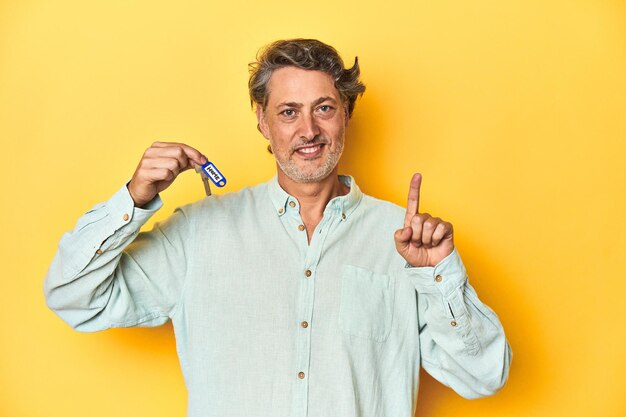 Man with new house keys on yellow backdrop showing number one with finger