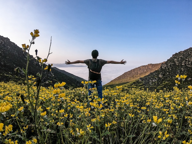 man with open arms standing over flower landscape of a mountainous valley