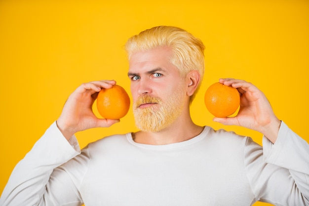 Man with oranges and orange juice in hands. Handsome young man hold fresh natural orange on orange backgroung isolated.