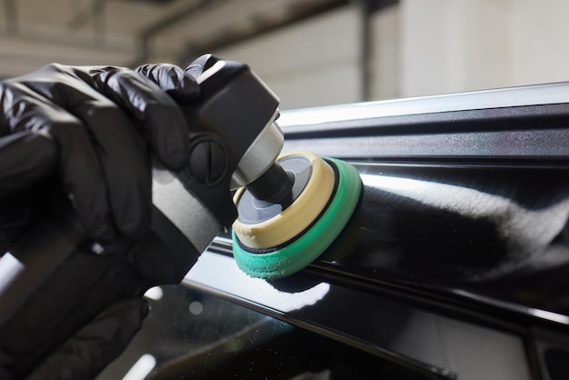 Man with an orbital polisher in car workshop polishing car closeup