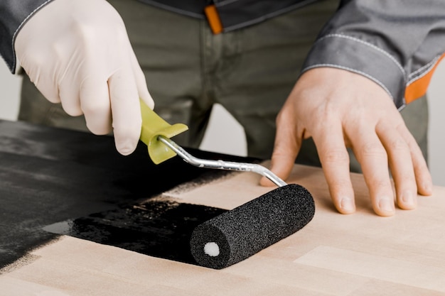 A man with a paint roller paints covers the wooden surface with
black paint the concept of the construction and repair