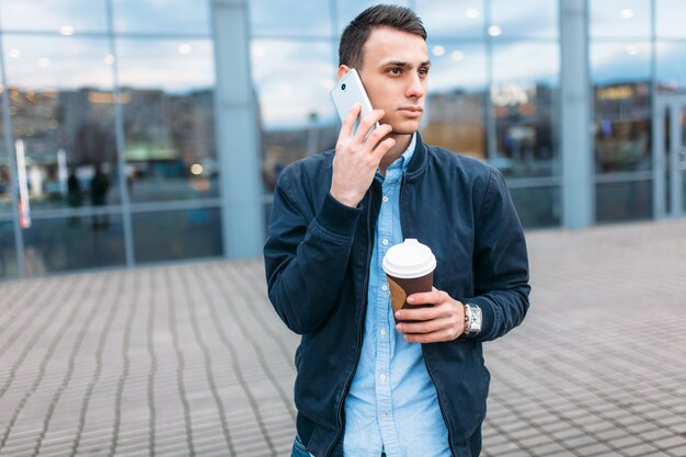 コーヒーの紙コップを持つ男は、電話でスタイリッシュな服を着たハンサムな男、街を通り抜けます