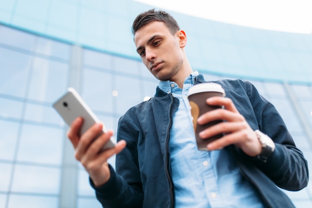 コーヒーの紙コップを持つ男は、電話を手にスタイリッシュな服を着たハンサムな男、街を通り抜けます