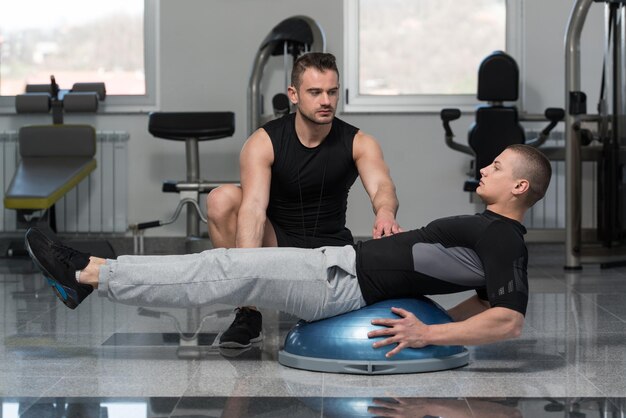 Man With Personal Trainer On Bosu Abs Exercise