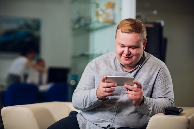 Man with phone being surprised as playing games sitting on sofa in office