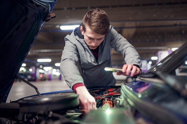 Man with phone in hand mending broken car with open hood