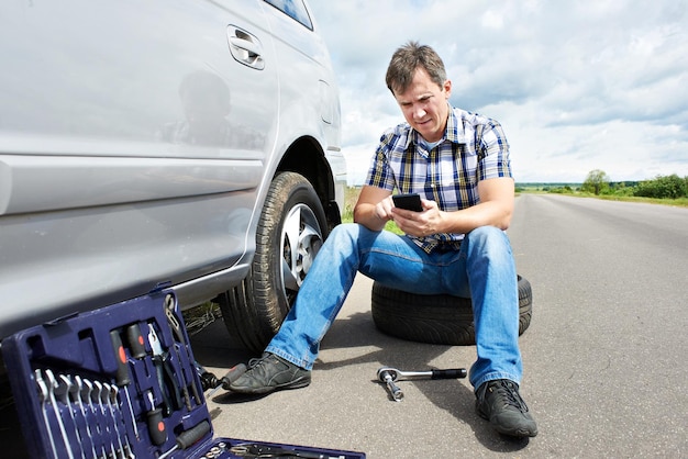 電話を持つ男がスペア タイヤ車のサービスで呼び出しています。