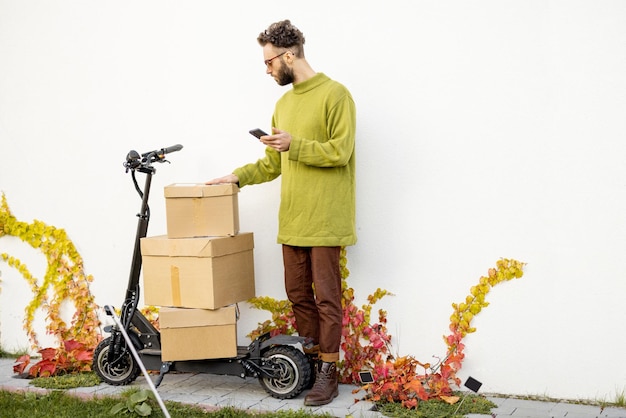 Man with phone near scooter and parcels outdooors