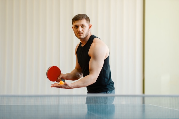 Человек с ракеткой для пинг-понга готовится ударить по мячу, тренировки в помещении.