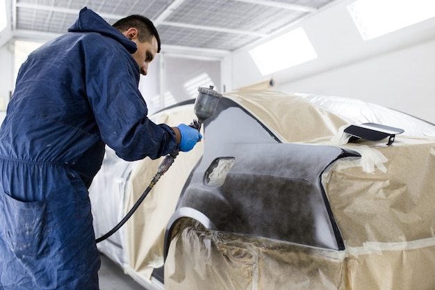 Man with protective clothes and mask painting car using spray compressor. Selective focus.