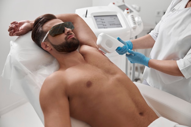 Мужчина в защитных очках и с обнаженной грудью проходит процедуру лазерной эпиляции подмышек