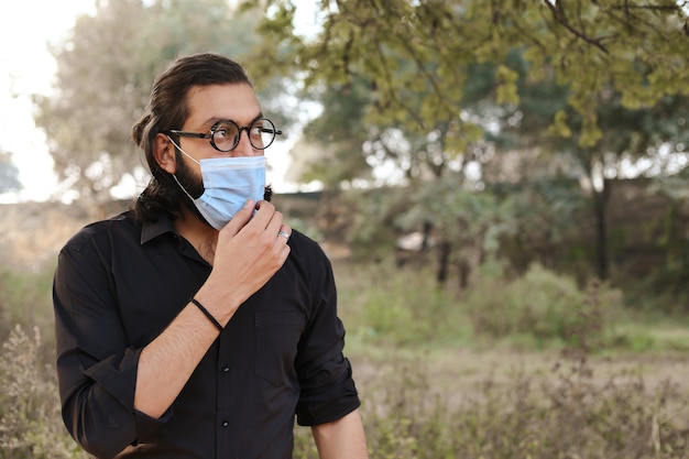 Man with a protective mask using a Mobile in nature