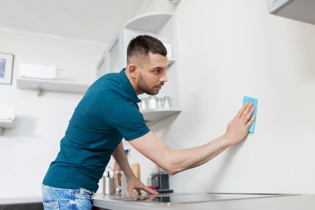 Photo man with rag cleaning wall at home kitchen