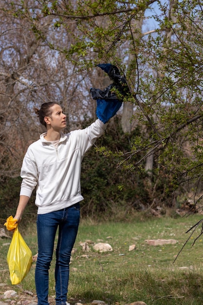 Photo man with a raised hand picking up garbage bag hooked on windblown tree