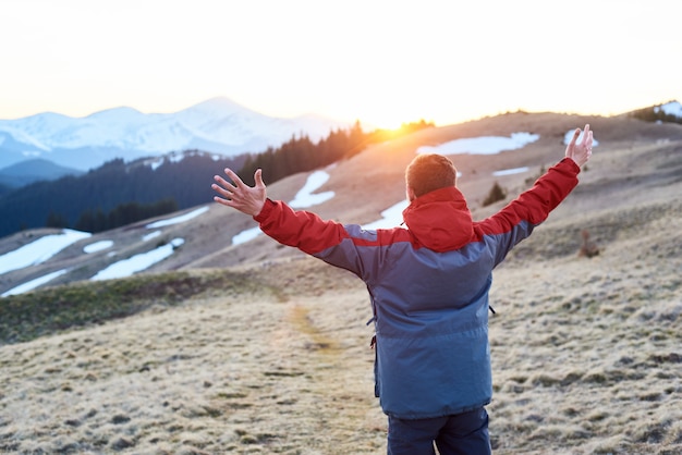 Man with raised hands watching beautiful scenery in mountains during colorful sunset